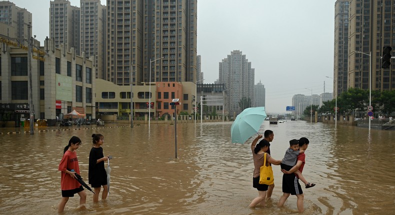 People wade across a flooded street following heavy rains which caused flooding and claimed the lives of at least 33 people earlier in the week, in the city of Zhengzhou in China's Henan province on July 23, 2021.
