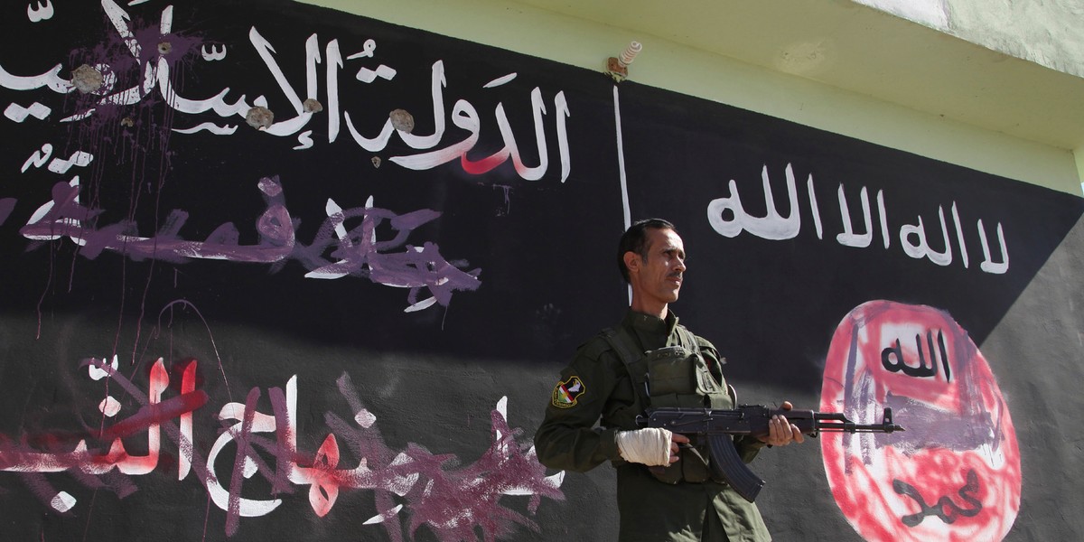 A Kurdish Peshmerga fighter stands near a wall on which the black flag commonly used by Islamic State militants have been painted over, in the northern Iraqi town of Zumar on October 26, 2014. The town had recently been retaken from the Islamic State.