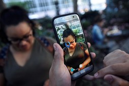 A Pokemon appears on the screen next to a woman as a man plays the augmented reality mobile game Pokemon Go by Nintendo in Bryant Park in New York City