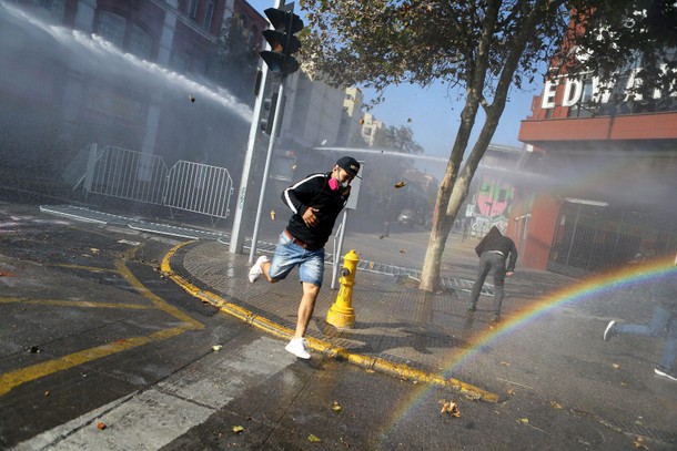 Demonstrators run away from a riot police water canon during a rally in Santiago