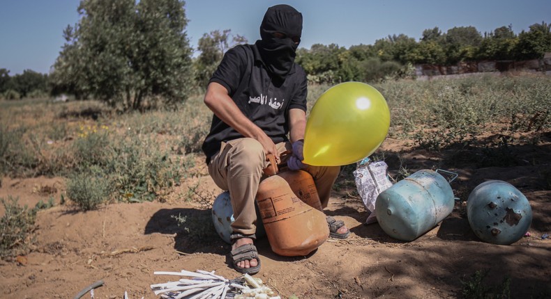 A masked Palestinian supporter of the Al-Nasir Salah Al-Din Brigades prepares incendiary balloons to launch across the border fence east of Gaza city towards Israel, on June 16, 2021 east of Gaza City in Gaza. The flare-up came after a controversial flag-waving march by Israeli nationalists was allowed to proceed through East Jerusalem on Tuesday, stoking tensions in Israel and Gaza less than a month after a ceasefire ended 11 days of fighting between Hamas and Israeli forces.
