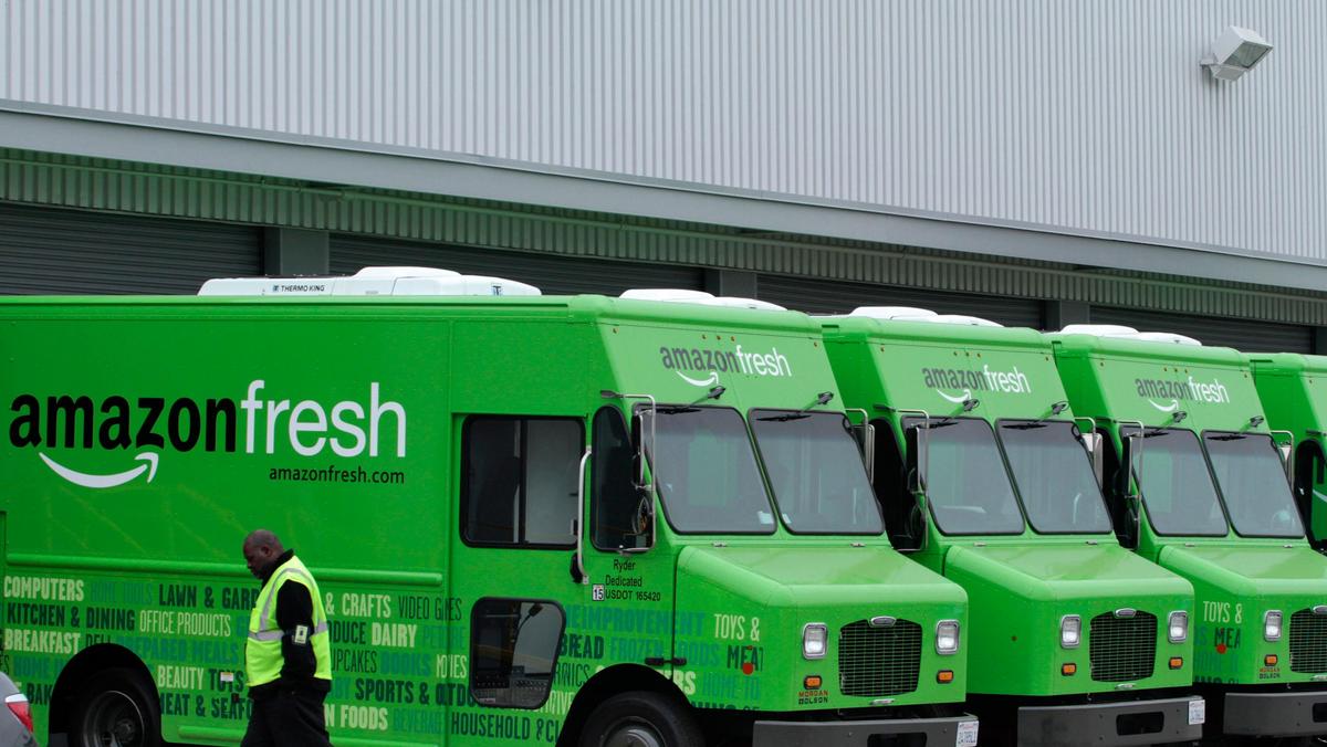 A worker walks past Amazon Fresh delivery vans parked at an Amazon Fresh warehouse in Inglewood