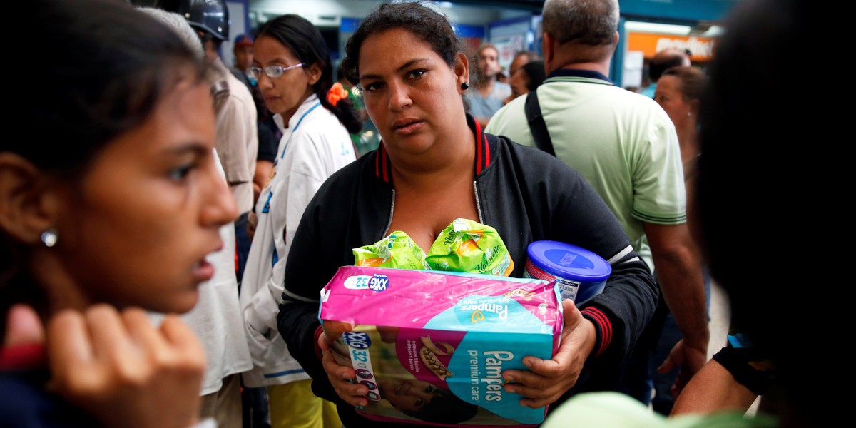 A woman holding food and other staple goods walks outside a supermarket in Caracas, Venezuela, June 30, 2016.