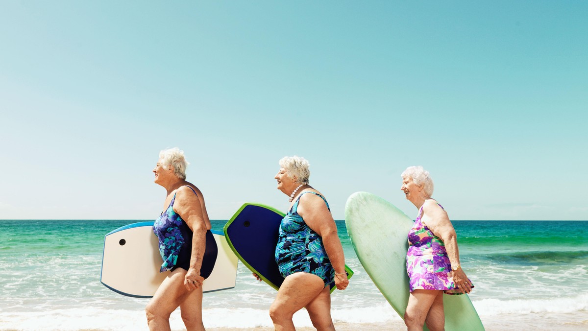 Three mature women on beach with surfboards