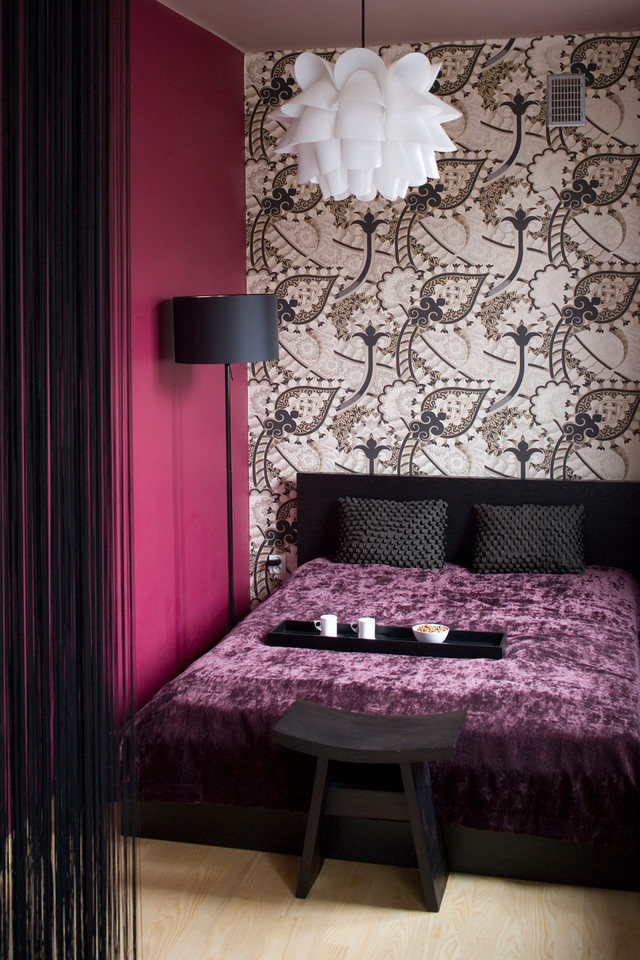 Sypialnia to wyspa koloru i ornamentów. Dookoła biel, a tu fioletowe ściany, zmysłowe tkaniny i dekoracyjna tapeta.