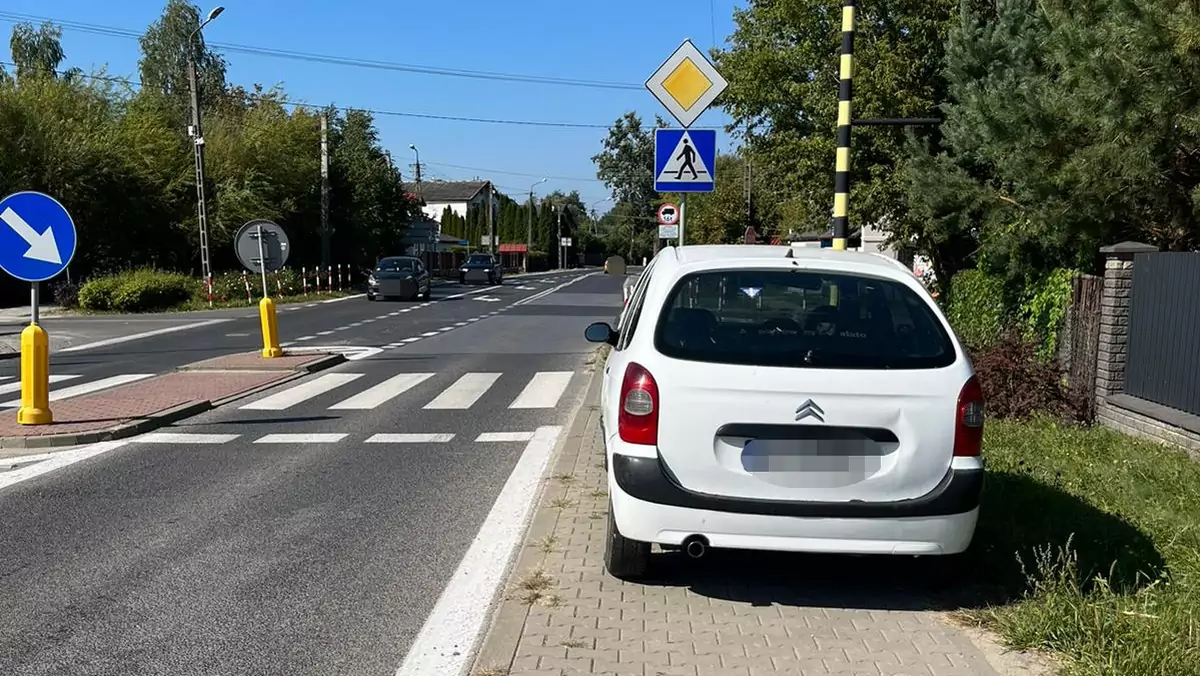 Biały Citroen zaparkowany na chodniku przed przejściem dla pieszych