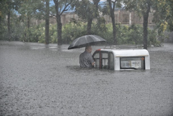 A man holding an umbrella trapped next to his vehicle on a flooded street in Beijing