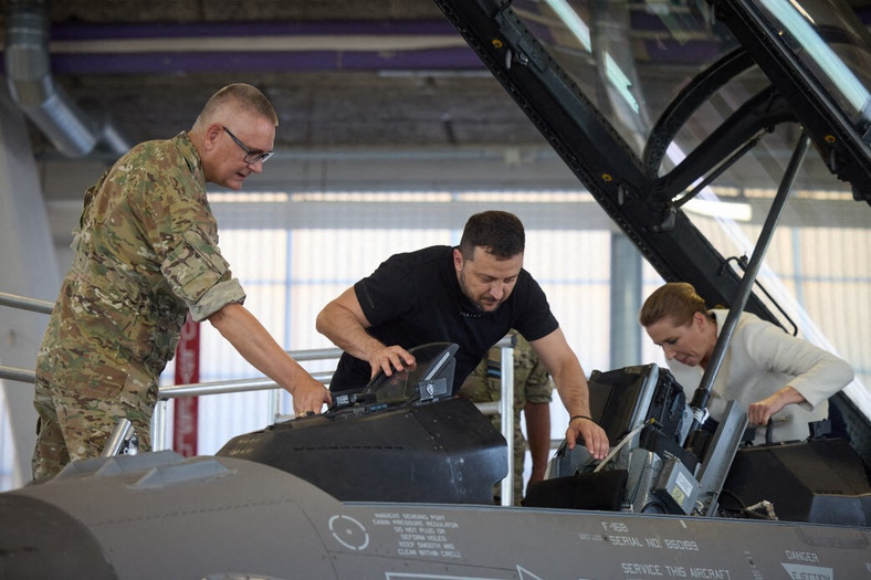 Prezydent Ukrainy Wołodymyr Zełenski (w środku) spotkał się z premier Danii Mette Frederiksen (po prawej) podczas wizyty w bazie lotniczej Fighter Wing Skrydstrup Królewskich Duńskich Sił Powietrznych podczas wizyty roboczej w Danii w sierpniu 2023 r. Podczas wizyty w bazie Zełenski obserwował odrzutowce F-16 i zapoznał się z możliwościami maszyn i specyfiką ich działania