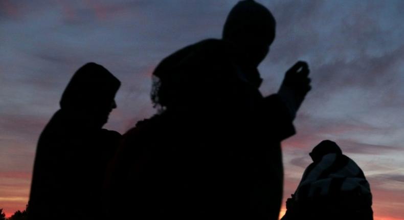 Migrants wait at dusk close to the Jungle migrant camp in Calais, northern France, on October 27, 2016, during a massive operation to clear the squalid settlement where 6,000-8,000 people have been living in dire conditions