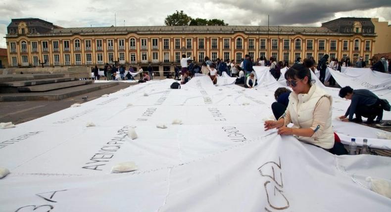 People sew white sheets with names of victims of the Colombian conflict painted in ash on them, in Bolivar square, Bogota