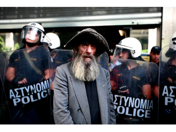 Bezdomny stojący na tle kordonu policji, podczas protestów pracowników Ministerstwa Finansów przed Ministerstwem Finansów w Atenach. Grecja, 27 września 2011