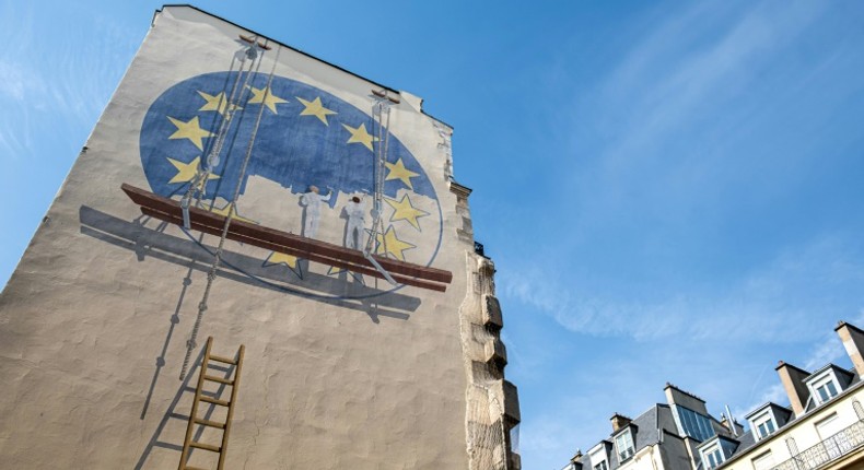 A trompe l'oeil shows two workers painting the European Union flag on the side of a building in Paris