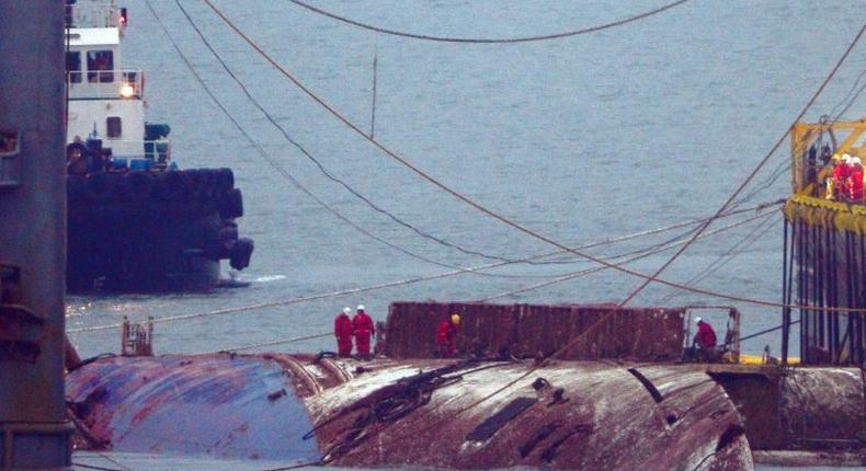 Workers check the hull of the Sewol ferry between two the barges that hauled it to the surface, nearly three years after it sank with the loss over 304 lives