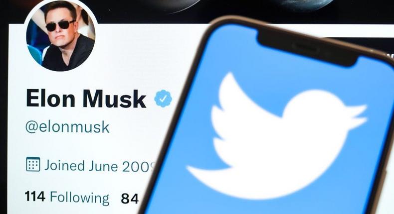 In this photo illustration, the Twitter logo is displayed on the screen of the phone, with Elon Musk's Twitter account in the background. (