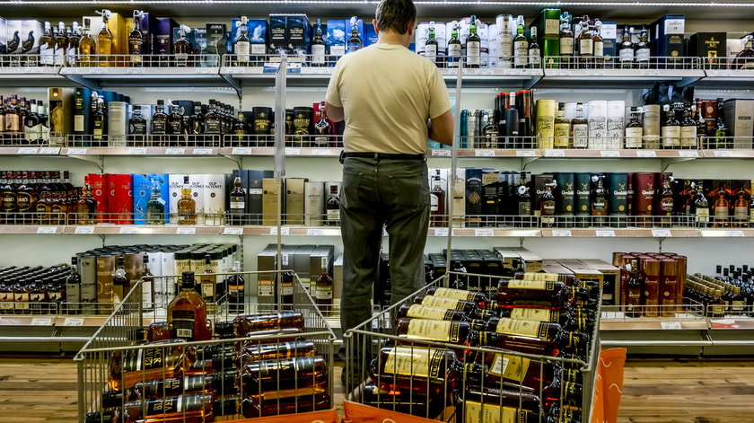 Mężczyzna w sklepie przed półkami z alkoholem. 