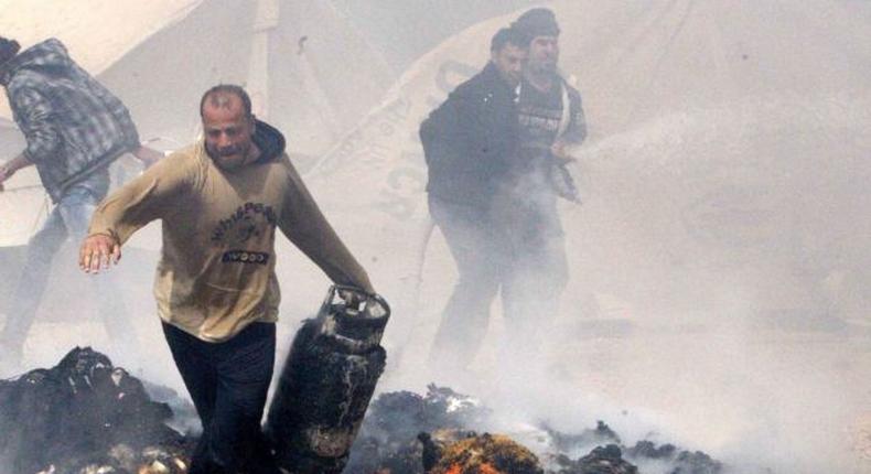 A Syrian refugee runs with a gas bottle cylinder, between burning tents.