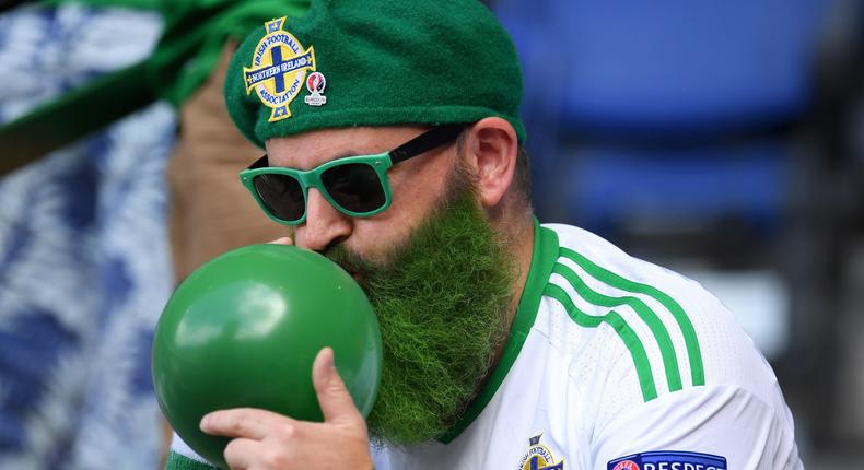 Man with a green beard blows up a balloon