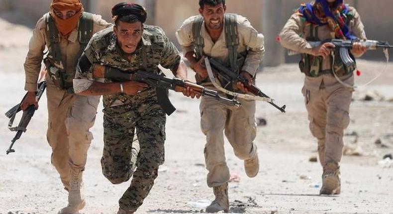 Kurdish fighters from the People's Protection Units (YPG) run across a street in Raqqa.