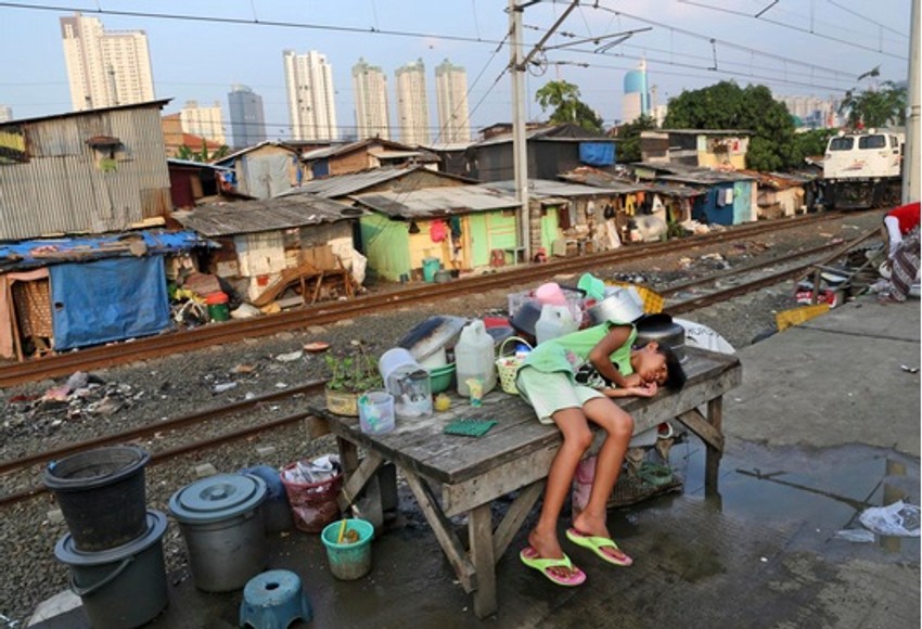 Devojčica leži na klupi u siromašnom naselju Džakarte, dok se u daljini vidi poslovni distrikt