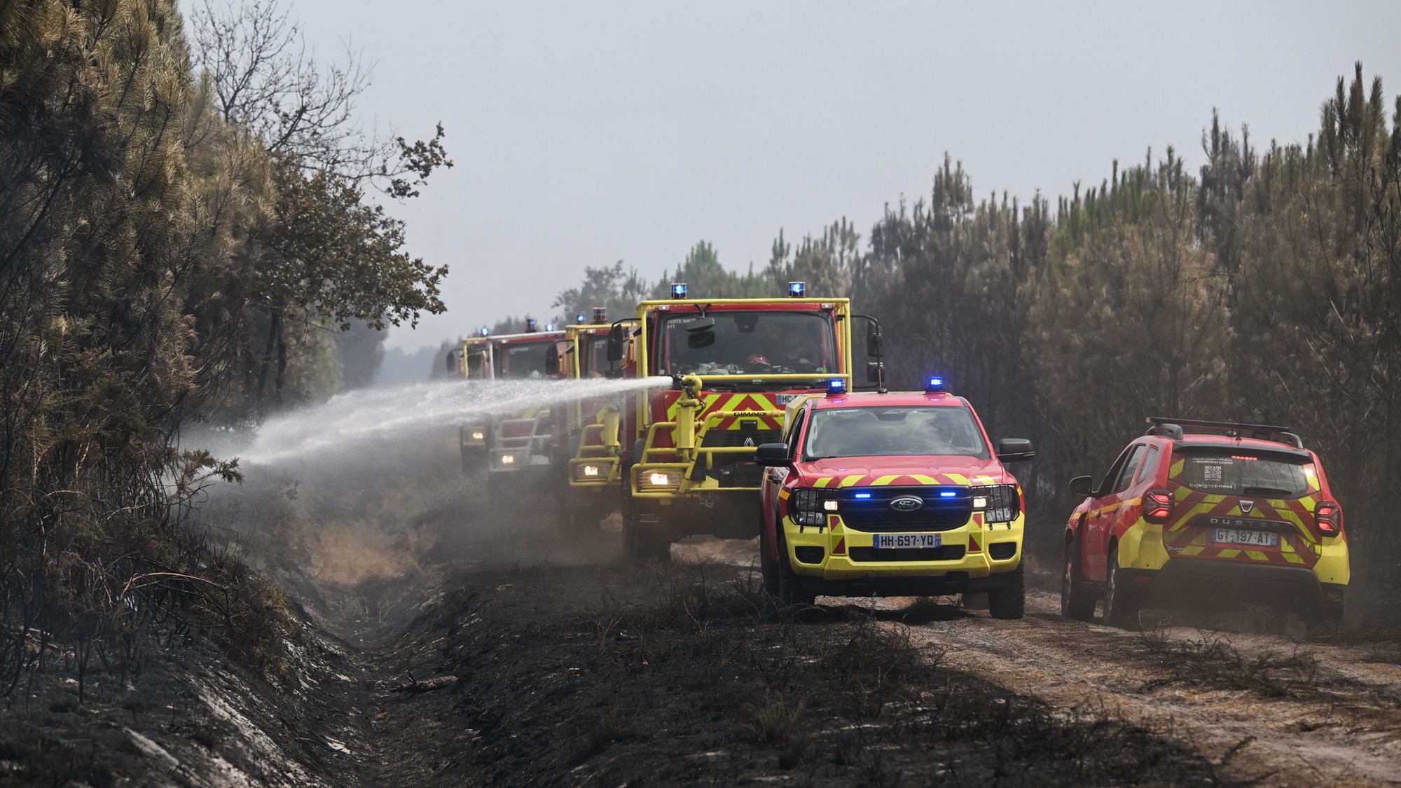 Hasiči polievajú kríky vodou počas lesných požiarov v obci Marcheprime neďaleko Bordeaux na juhozápade Francúzska.