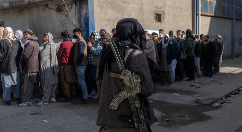 A Taliban fighter secures the area as people queue to receive cash at a money distribution site organized by the World Food Programme in Kabul, Afghanistan.