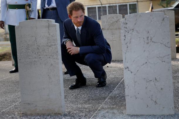 Britain's Prince Harry kneels down to read headstones at a cemetery during an official visit of Geor