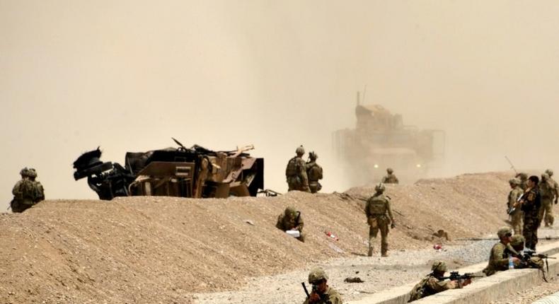 US soldiers keep watch near the wreckage of their vehicle at the site of a Taliban suicide attack in Kandahar on August 2, 2017