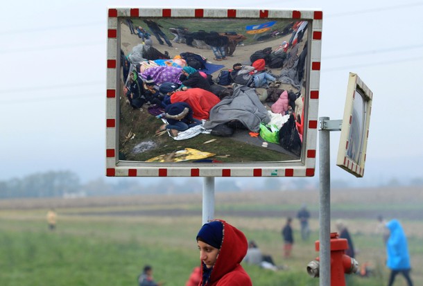 A girl looks on as resting migrants are seen in a street mirror after crossing the border from Croat