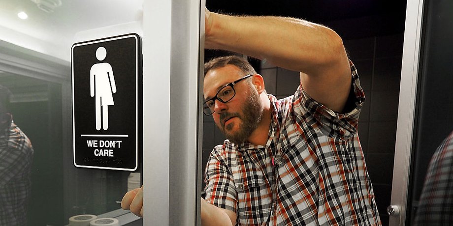 Museum manager Jeff Bell adheres informative backing to gender neutral signs in the 21C Museum Hotel public restrooms on May 10, 2016 in Durham, North Carolina.