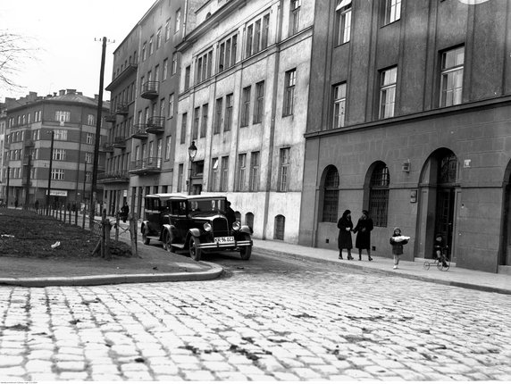 Aleja Słowackiego od nr 60 do 66. Widoczne na ulicy dwa samochody osobowe, na chodniku dwie kobiety z dziewczynką i chłopcem jadącym na trzykołowym rowerze (1934 r.)