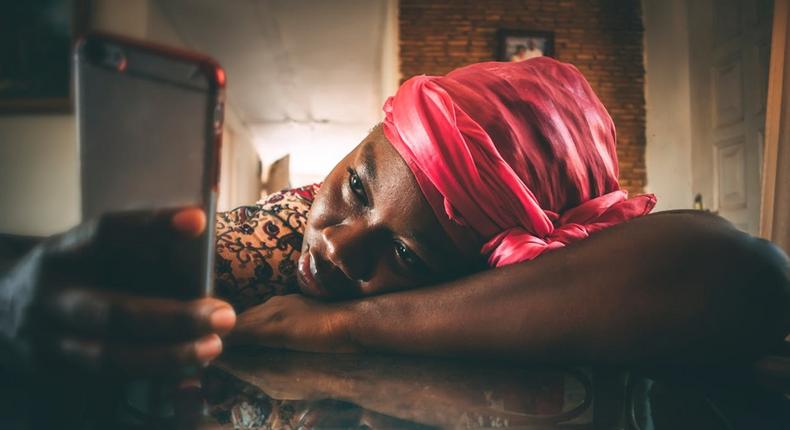 A woman in a headwrap and dera using her phone [Image Credit: Ekua Apau]