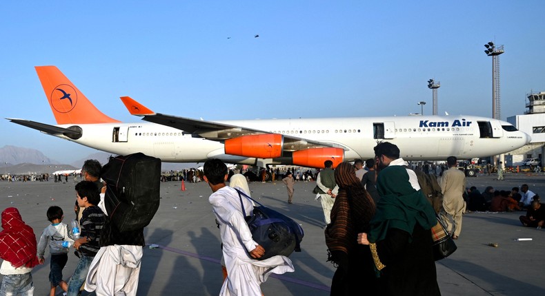 Afghan families walk by the aircrafts at the Kabul airport in Kabul on August 16, 2021, after a stunningly swift end to Afghanistan's 20-year war, as thousands of people mobbed the city's airport trying to flee the group's feared hardline brand of Islamist rule.
