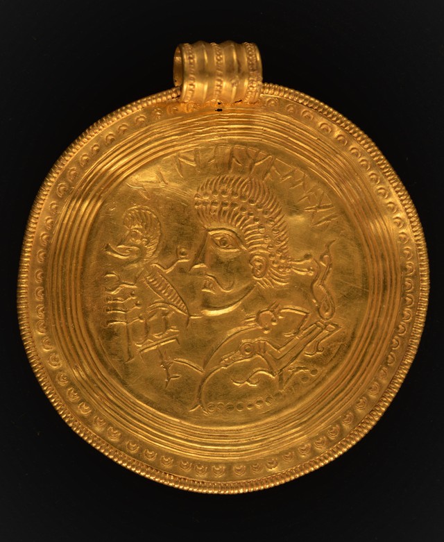A medallion, known as a bracteate, featuring the face of a man and runes.