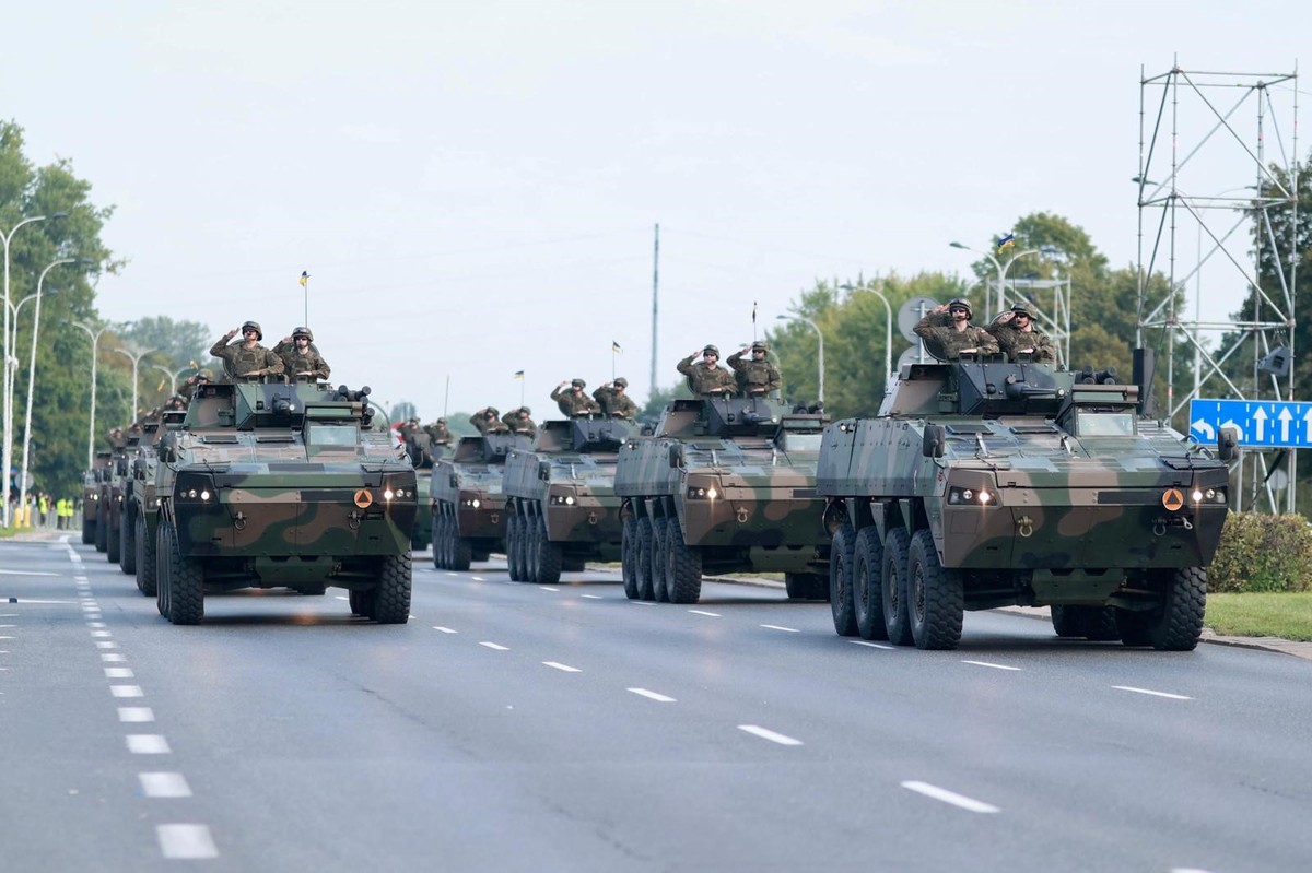 Zdjęcie przedstawia kolumnę wojskowych pojazdów opancerzonych Rosomak jadących po szerokiej, zamkniętej dla ruchu ulicy w Warszawie podczas próby generalnej przed defiladą z okazji Święta Wojska Polskiego 15 sierpnia. Na pojazdach stoją żołnierze.