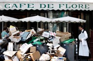 A waiter stands near a pile of rubbish bags in front of the Cafe de Flore in Paris during a strike of garbage collectors and sewer workers of the city of Paris to protest the labour reforms law proposal