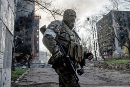 Rosyjski żołnierz stoi na tle płonącego bloku mieszkalnego w centrum Mariupola. Ukraina, 18.04.2022