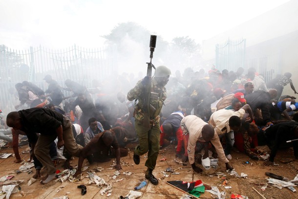 People fall as police fire tear gas to try control a crowd trying to force their way into a stadium 