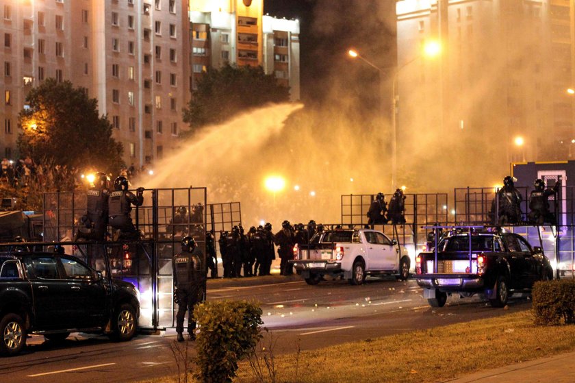 A law enforcement officer kneels next to a man laying on the ground during clashes with opposition s