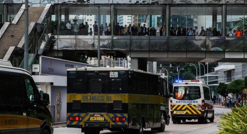 Bystanders watch as a prison van (C) transporting British banker Rurik Jutting, accused of the murders of two Indonesian women, leaves the High Court escorted by a police convoy in Hong Kong in the city's biggest murder case for years