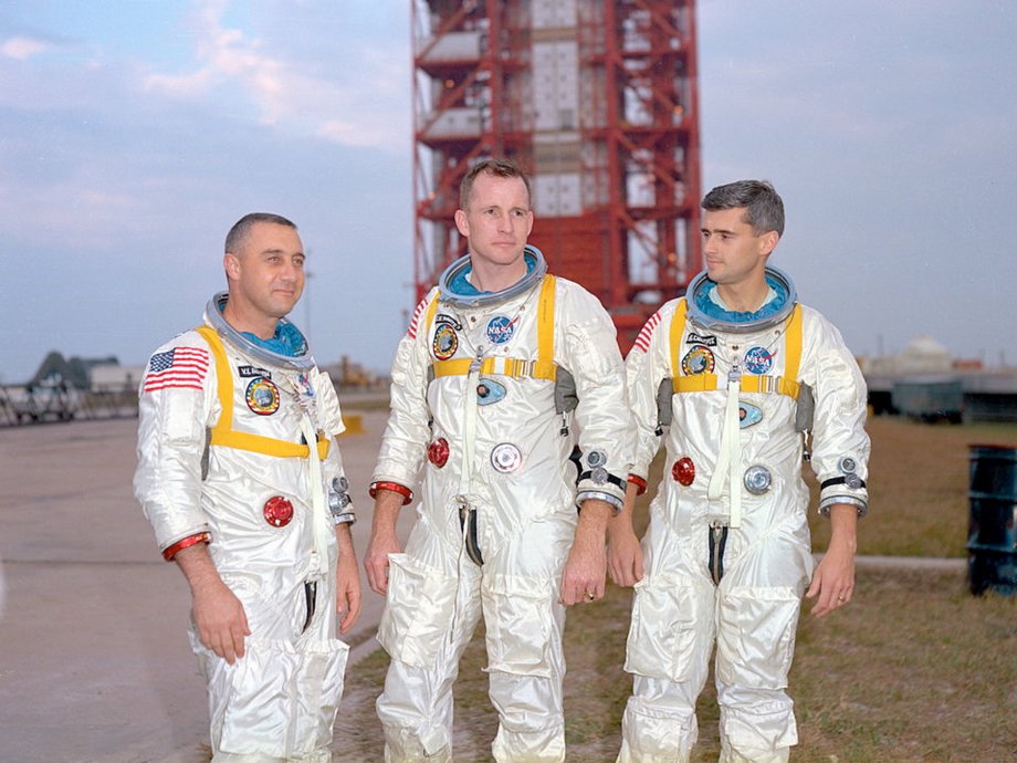 Astronauci Apollo 1 od lewej: Virgil "Gus" Grissom, Edward White i Roger Chaffee. W tle rakieta Saturn 1 w Centrum Kosmicznym Kennedy'ego. Astronauci zginęli podczas rutynowego testu