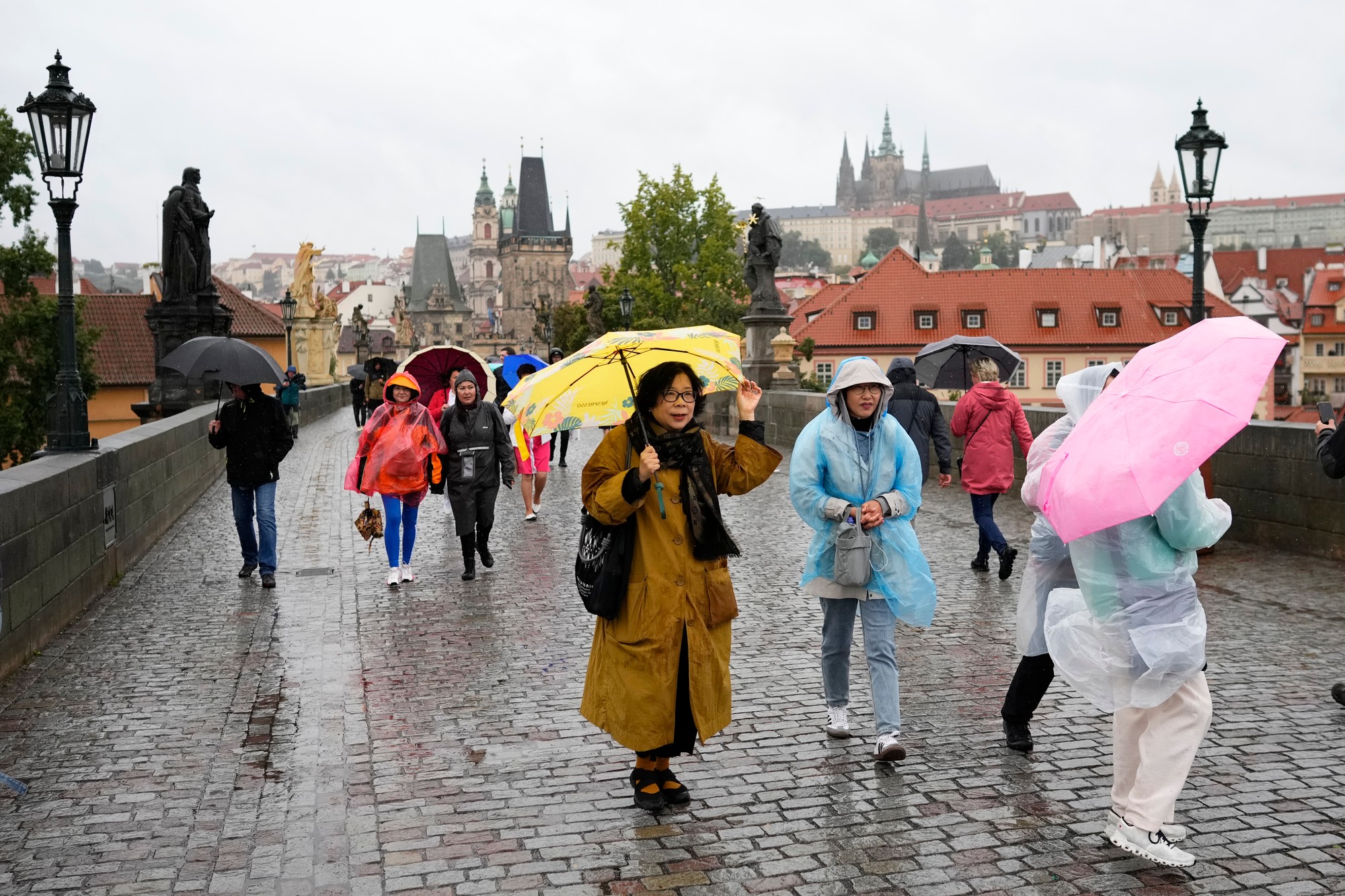 Ľudia s dáždnikmi kráčajú po Karlovom moste v Prahe 13. septembra 2024 počas daždivého počasia.