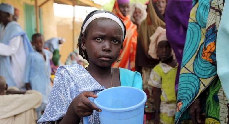 A girl drinks water as women queue for blankets and food given out by Nigerien soldiers in Damasak