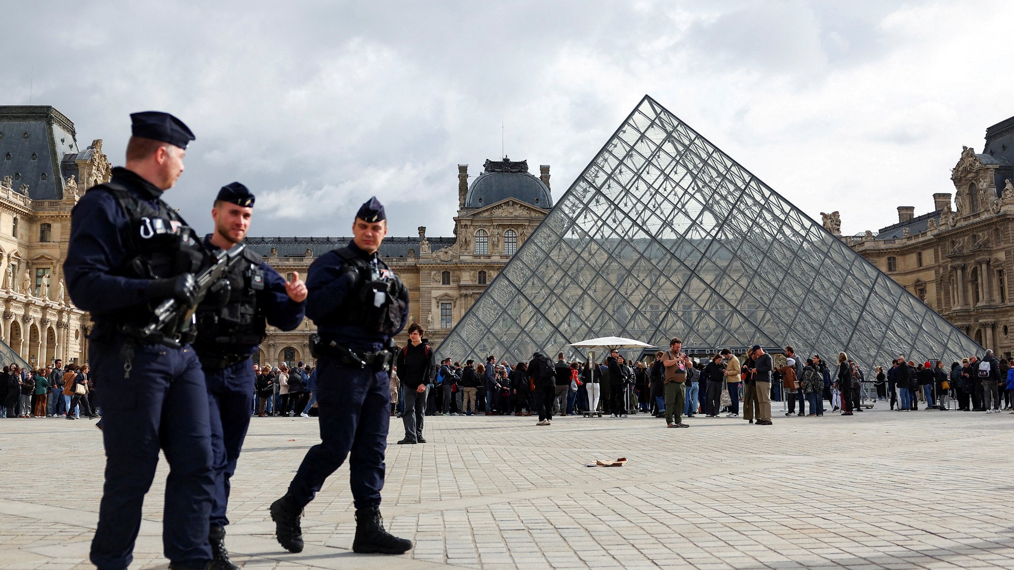 Francúzski policajti CRS v protivýtržnom výstroji kráčajú v blízkosti sklenenej pyramídy múzea Louvre.