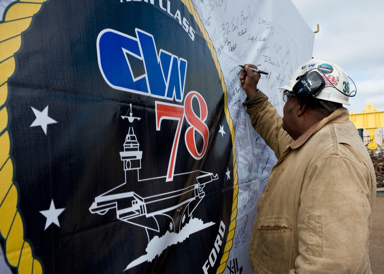 John Knight, operator dźwigu, podpisuje baner lotniskowca Gerald R. Ford (CVN 78), wystawiony później na ceremonii montażu stępki okrętu , fot. Ricky Thompson, materiały prasowe Huntington Ingalls Industries