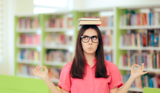 stock-photo-funny-student-balancing-books-over-her-head-in-a-library-cute-academic-girl-managing-anxiety-before-1134309806
