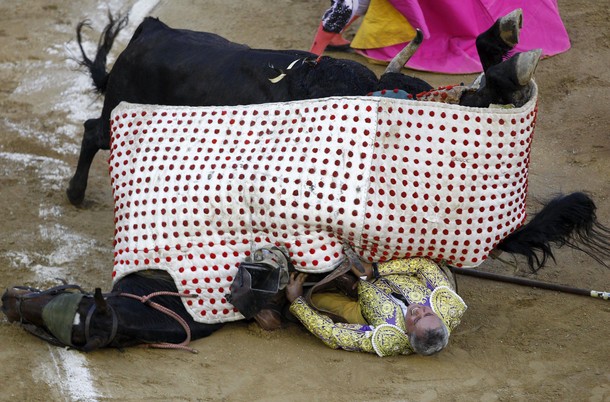 Picador Diego Ochoa reacts while being pinned under a horse as a bull charges at it during a bullfig