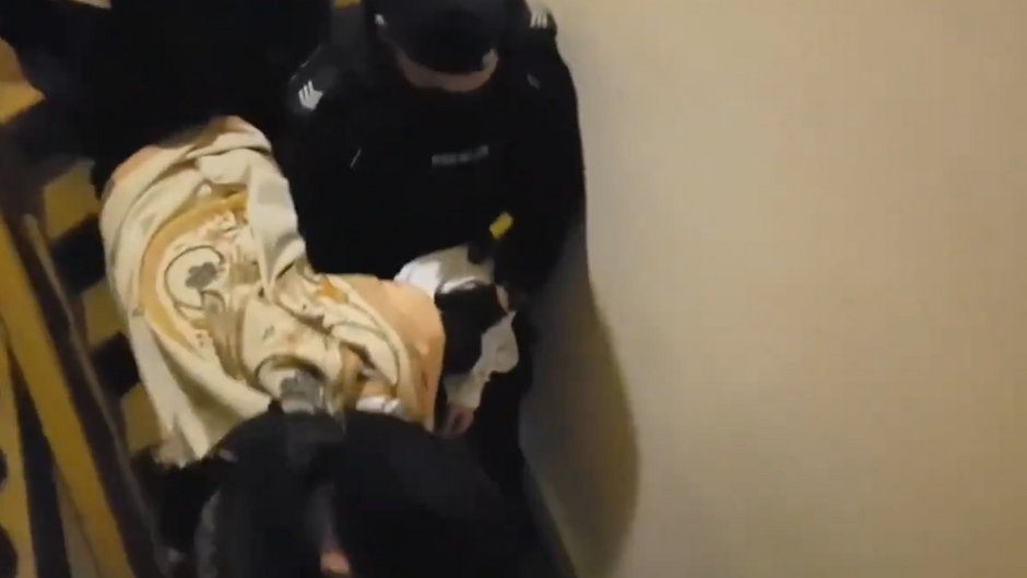 Policjanci doprowadzają ks. Michała Woźnickiego do komisariatu (kadr z nagrania)