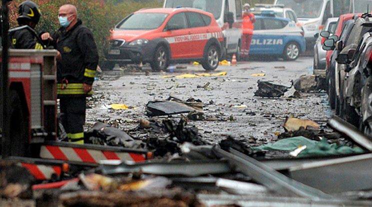 Tűzoltók állnak megrongálódott autók mellett a repülőgép-szerencsétlenség helyszínén Milánó külvárosában 2021. október 3-án, miután egy öt utast és egy pilótát szállító kisrepülőgép egy irodaházra zuhant. A balesetet senki sem élte túl / Fotó: MTI/AP/LaPresse/Claudio Furlan