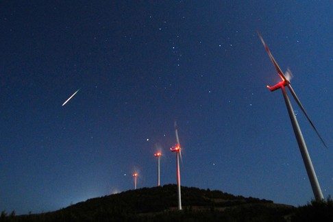 A meteor streaks across the sky during the Perseid meteor shower at a windmill farm near Bogdanci