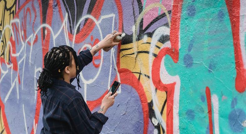 A woman doing graffiti on a wall using a spray paint [Image Credit: Felicity Tai]